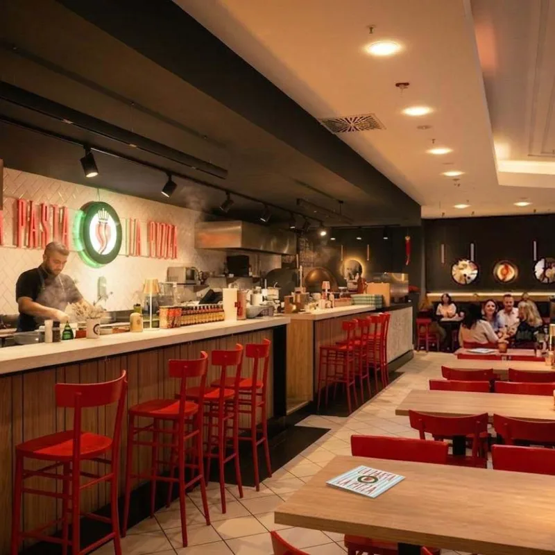 OVEST Restaurant in der 6. Etage des KaDeWe Berlin – offene Küche, rote Stühle und La Pasta La Pizza Leuchtschrift
